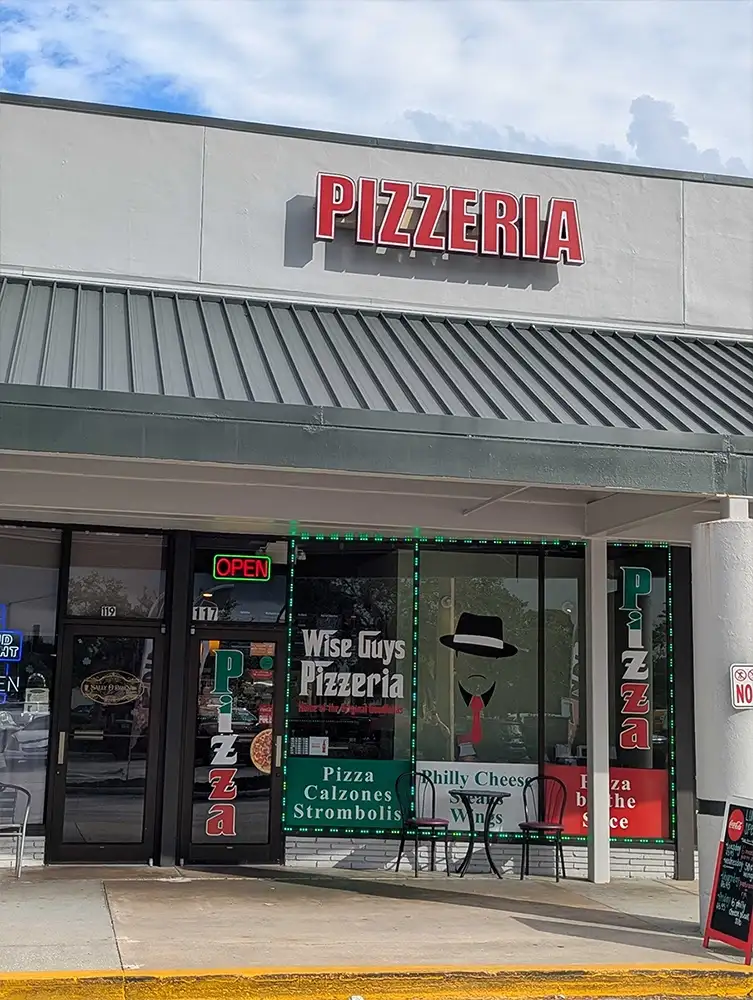 Exterior of Wise Guys Pizzeria in Florida, featuring signage and storefront with pizza and calzone offerings displayed