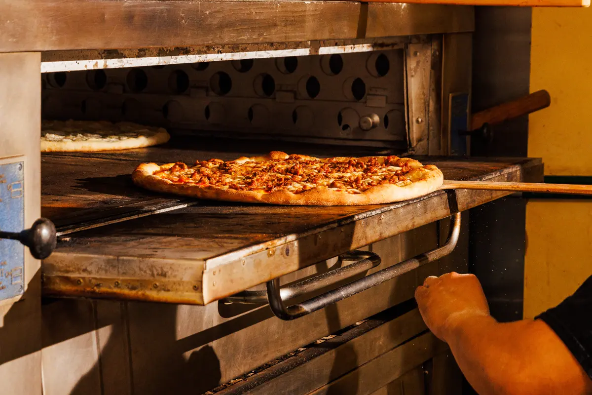 Chef putting a pizza into a commercial oven at WiseGuys Pizza