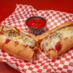 Delicious wood-fired pizza with melted cheese, herbs, and a side of marinara sauce on a red and white checkered tablecloth