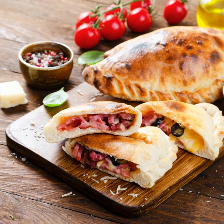Golden baked calzone sliced open showing meat and cheese filling on wooden board with marinara sauce