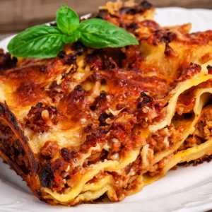 A hearty slice of Wise Guys Pizza Lasagna, featuring layers melted cheese, savory tomato sauce, and fresh basil garnish