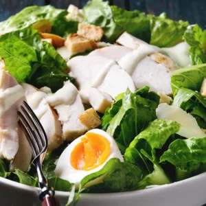 A large bowl filled with a fresh salad featuring lettuce, chicken, hard-boiled egg, and other vegetables